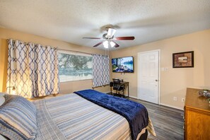 A bedroom with a bed, curtains, a ceiling fan, a television, a desk, and a door. - Serene Lakeside 2BR | Sunset Views & Relaxing Stay (Montgomery)