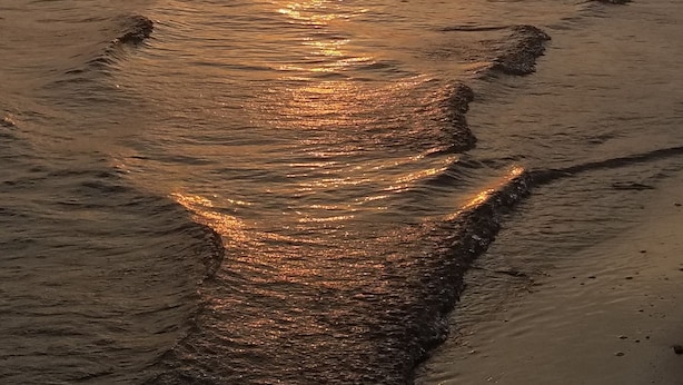 A sunset over a beach with a visible path of wet sand leading towards the water.