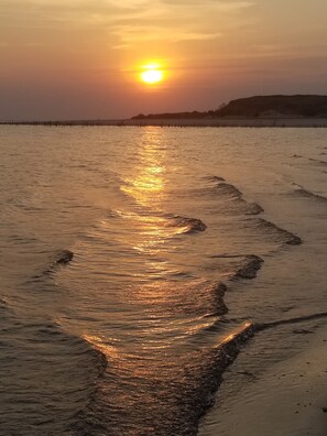 Ein Sonnenuntergang über einem Strand, wo eine feuchte Sandspur zum Wasser führt.