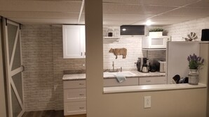A kitchen with white cabinets, a brick wall, a wooden cow decoration, and a coffee maker.