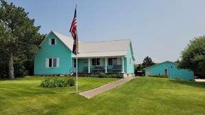 A turquoise house with a porch, a flagpole with an American flag, and a small shed.