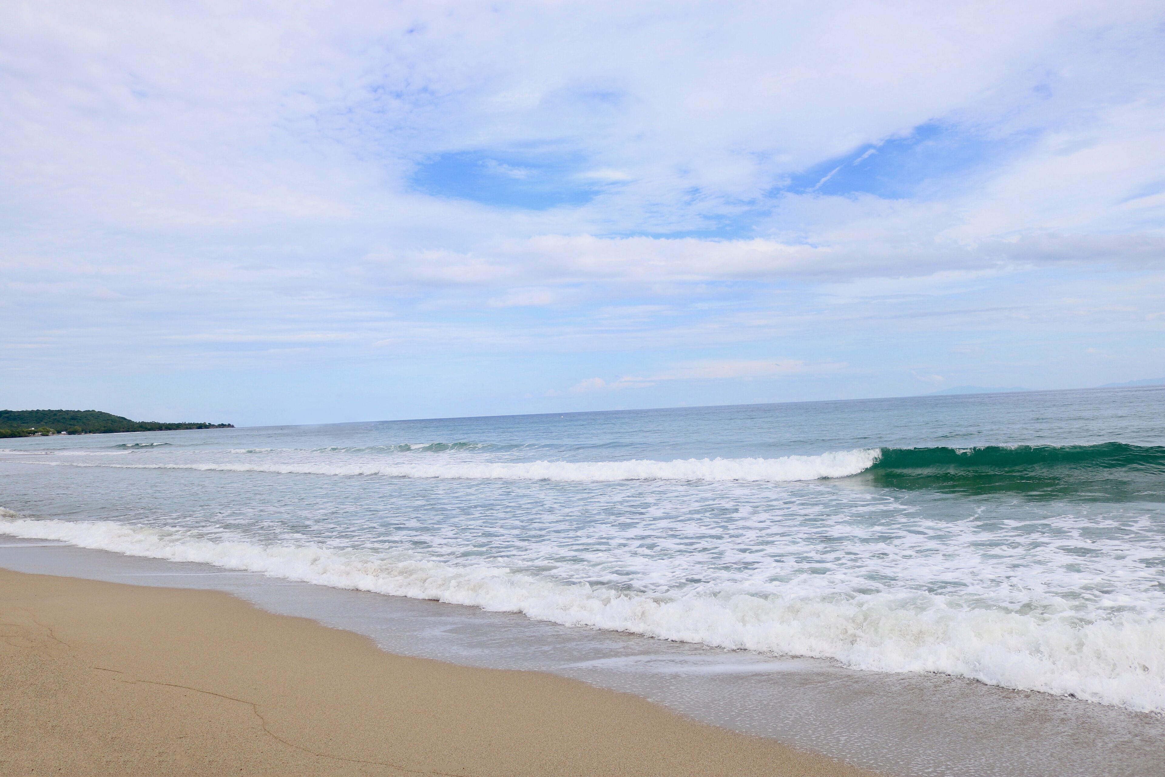 Ein Strand mit Wellen, wolkenlosem Himmel und einer entfernten Landmasse.