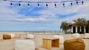 A beach setting with bean bags, a wooden table, and string lights. - Cocoons Club Laiya (San Juan)