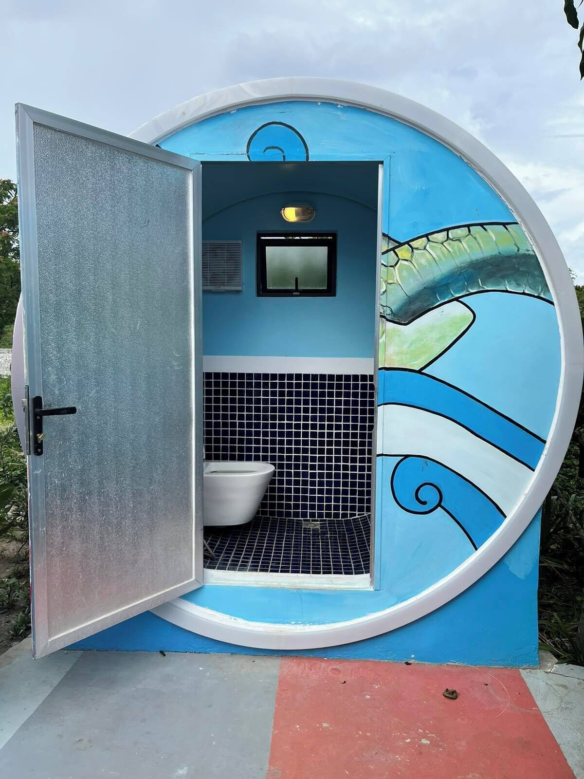 Une salle de bain circulaire aux couleurs bleu et blanc, comprenant des toilettes, une petite fenêtre et un mur décoratif.