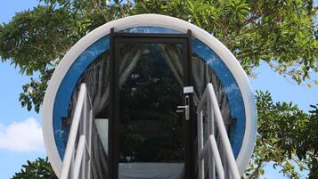 A circular structure with a door and steps leading up to it, surrounded by trees.