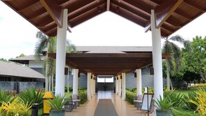 A covered walkway with a wooden roof, white pillars, and a view of a building in the background. - Cocoons Club Laiya (San Juan)