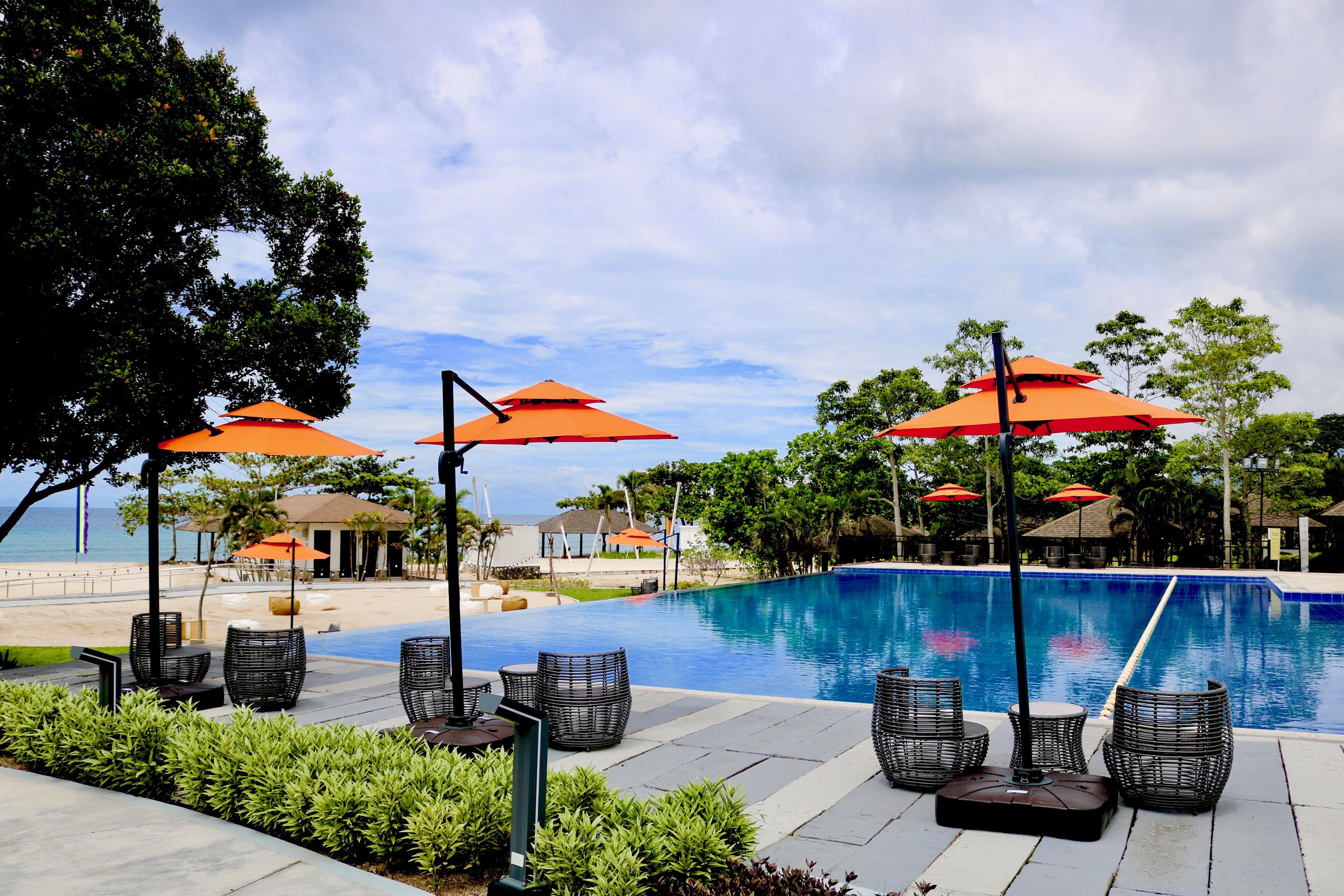 A poolside area with lounge chairs and umbrellas, a clear sky, and a view of the beach.