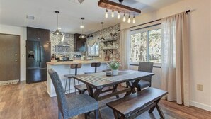 A modern kitchen with a central island, pendant lighting, and a large window with curtains. - Elkchanted Inn Pine: Fully Fenced Backyard, Spacious Cabin in Woods w/King Bed (Pine)