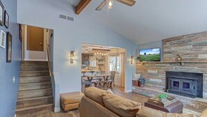 A cozy living room with a stone fireplace, a comfortable leather sofa, and a dining area with a table and chairs. - Elkchanted Inn Pine: Fully Fenced Backyard, Spacious Cabin in Woods w/King Bed (Pine)