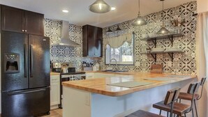 A modern kitchen with a central island, dark cabinetry, and patterned wallpaper. - Elkchanted Inn Pine: Fully Fenced Backyard, Spacious Cabin in Woods w/King Bed (Pine)