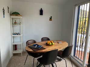 Un comedor con una mesa de madera, sillas negras, un frutero y un estante blanco decorado.