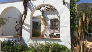 A white building with arches, a vine, and a window with a metal grille. - Holiday Home "Cortijo Pura Vida" with Mountain View, Pool, Terrace & Garden (Cómpeta)