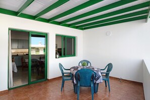 Un espace repas comprenant une table et des chaises, une porte-fenêtre coulissante et une fenêtre à cadre vert.