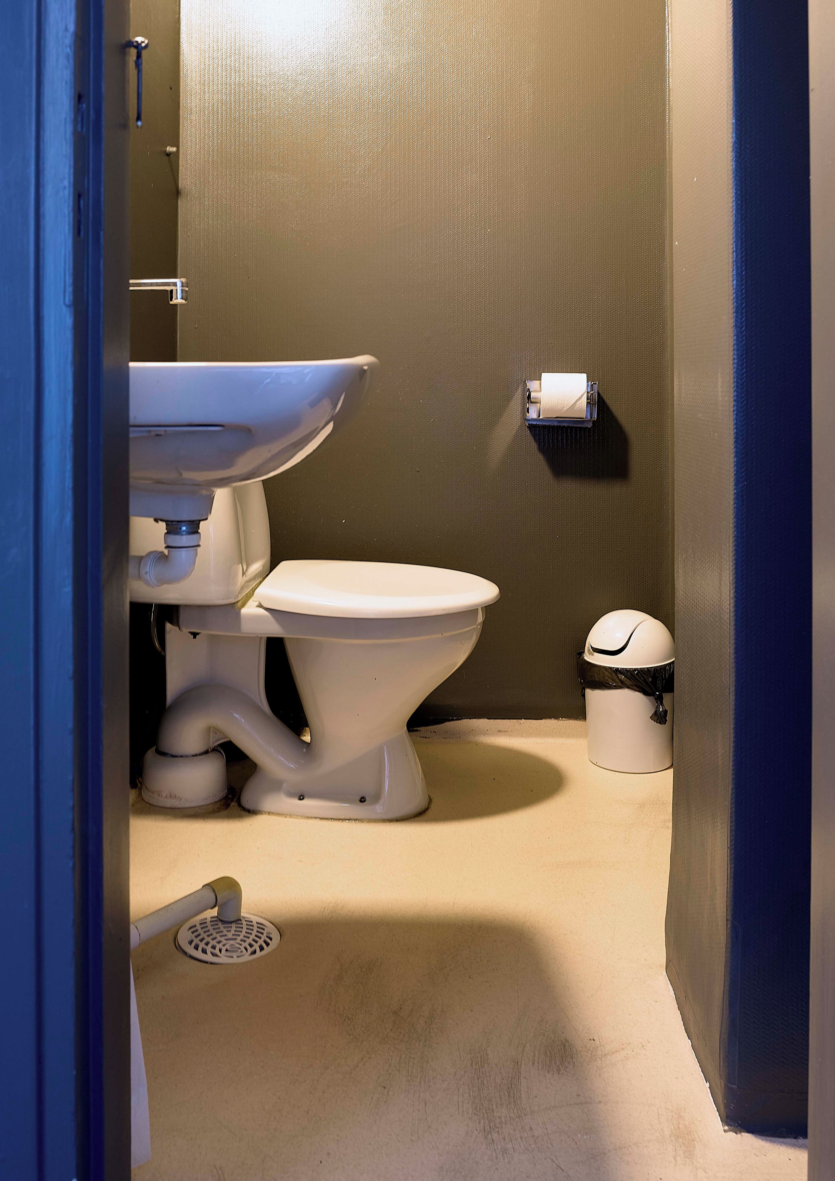 A bathroom with a toilet, sink, and trash can.