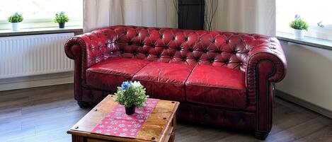 A red leather sofa with a floral table runner and a potted plant in front.