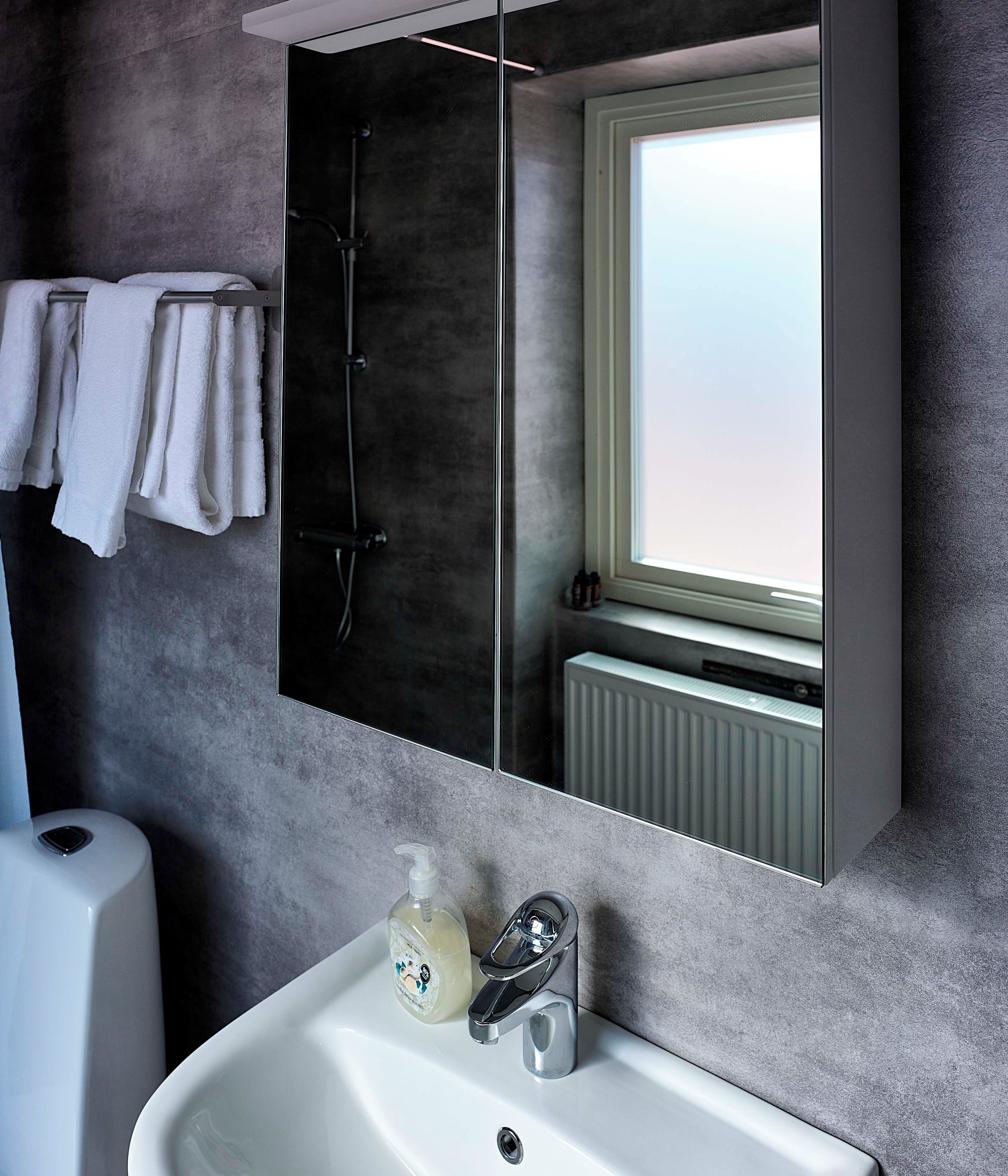 Ein modernes Badezimmer mit einem großen Spiegel, einem weißen Waschbecken und einem Handtuchhalter.