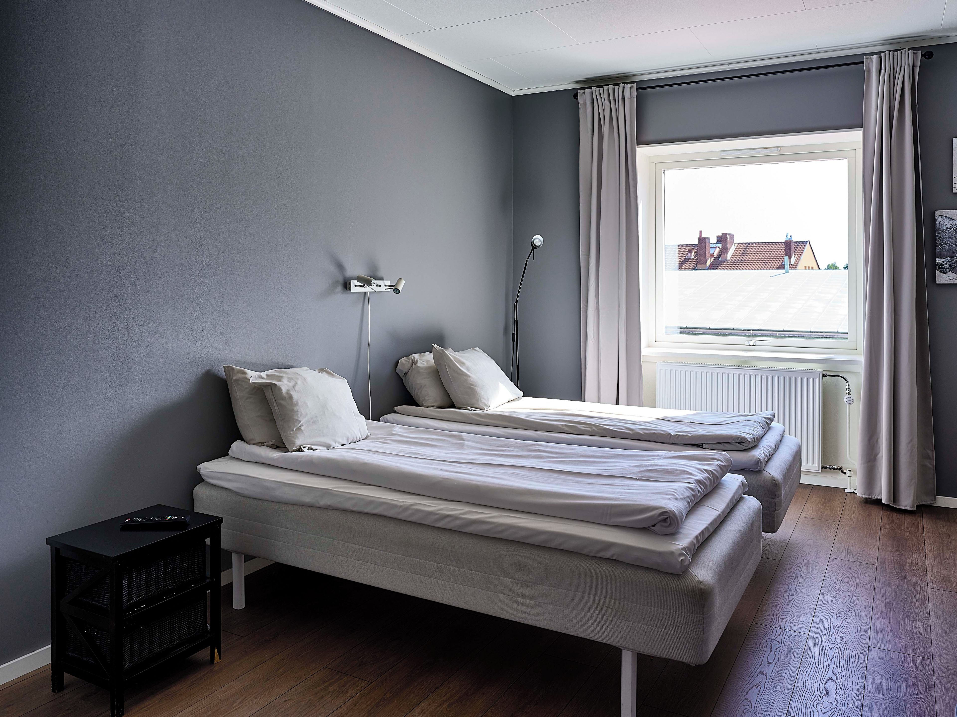 Ein Schlafzimmer mit zwei Betten, einem Nachttisch, einer Lampe und einem Fenster mit Vorhängen.