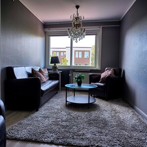 A living room with a dark leather sofa, a round coffee table, and a chandelier. - Saga Hotell AB (Borlange)