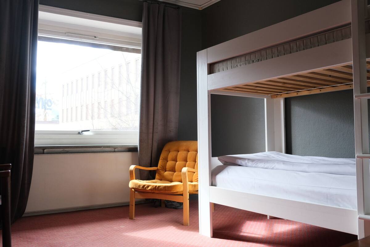 Une chambre avec un lit superposé, une chaise et une fenêtre.