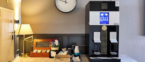 Zona de recepción de un hotel con un reloj, una máquina de café y una lámpara.