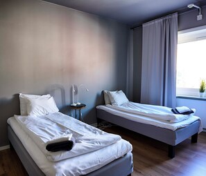 A hotel room with two single beds, a bedside table with a lamp, and a window with curtains. - Saga Hotell AB (Borlange)