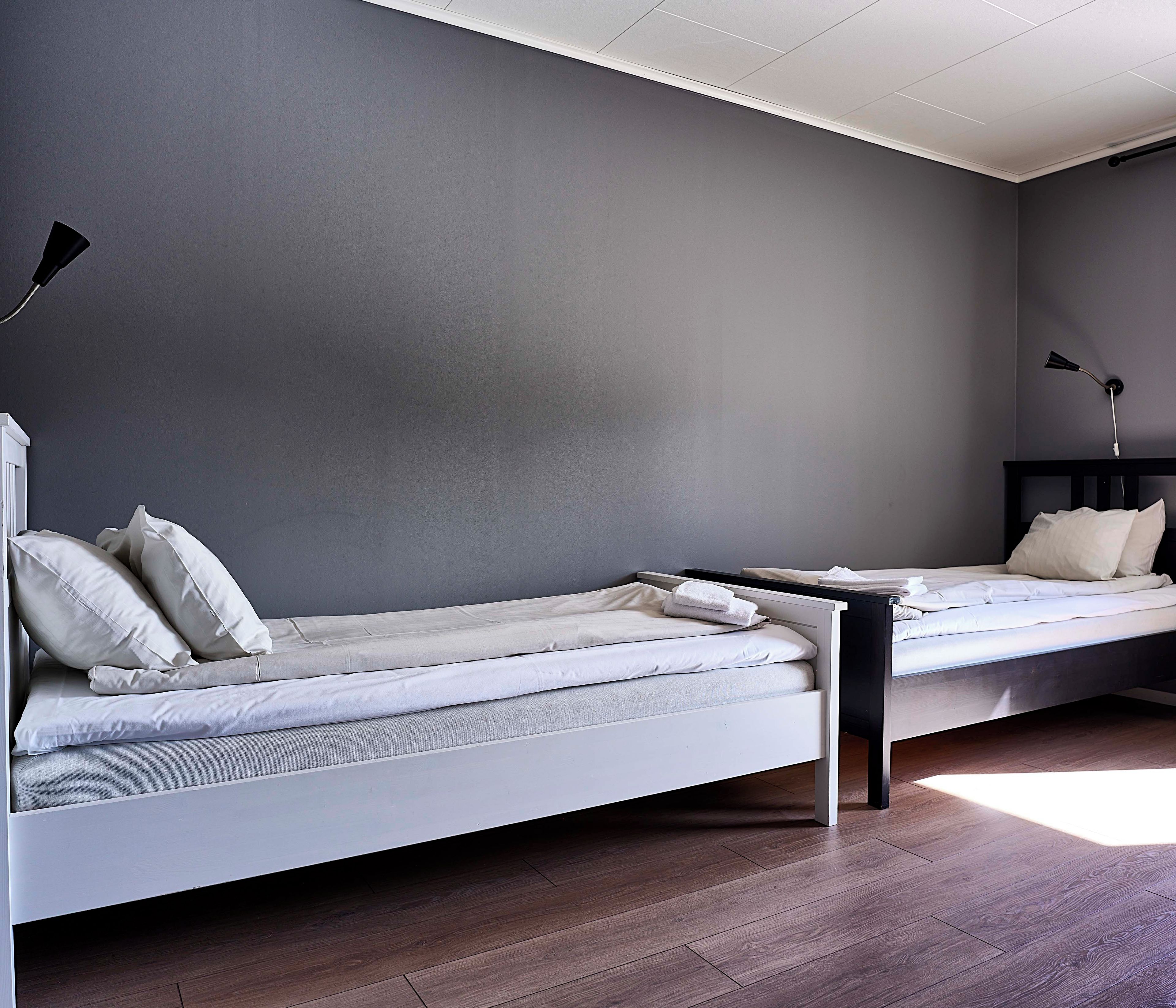Un dormitorio moderno con dos camas individuales, una mesita de noche, una lámpara y suelo de madera.