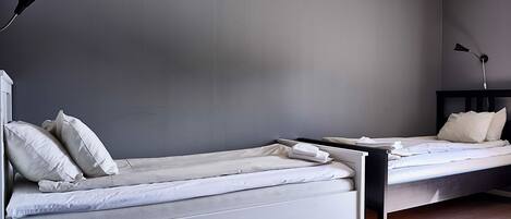 Un dormitorio moderno con dos camas individuales, una mesita de noche, una lámpara y suelo de madera.