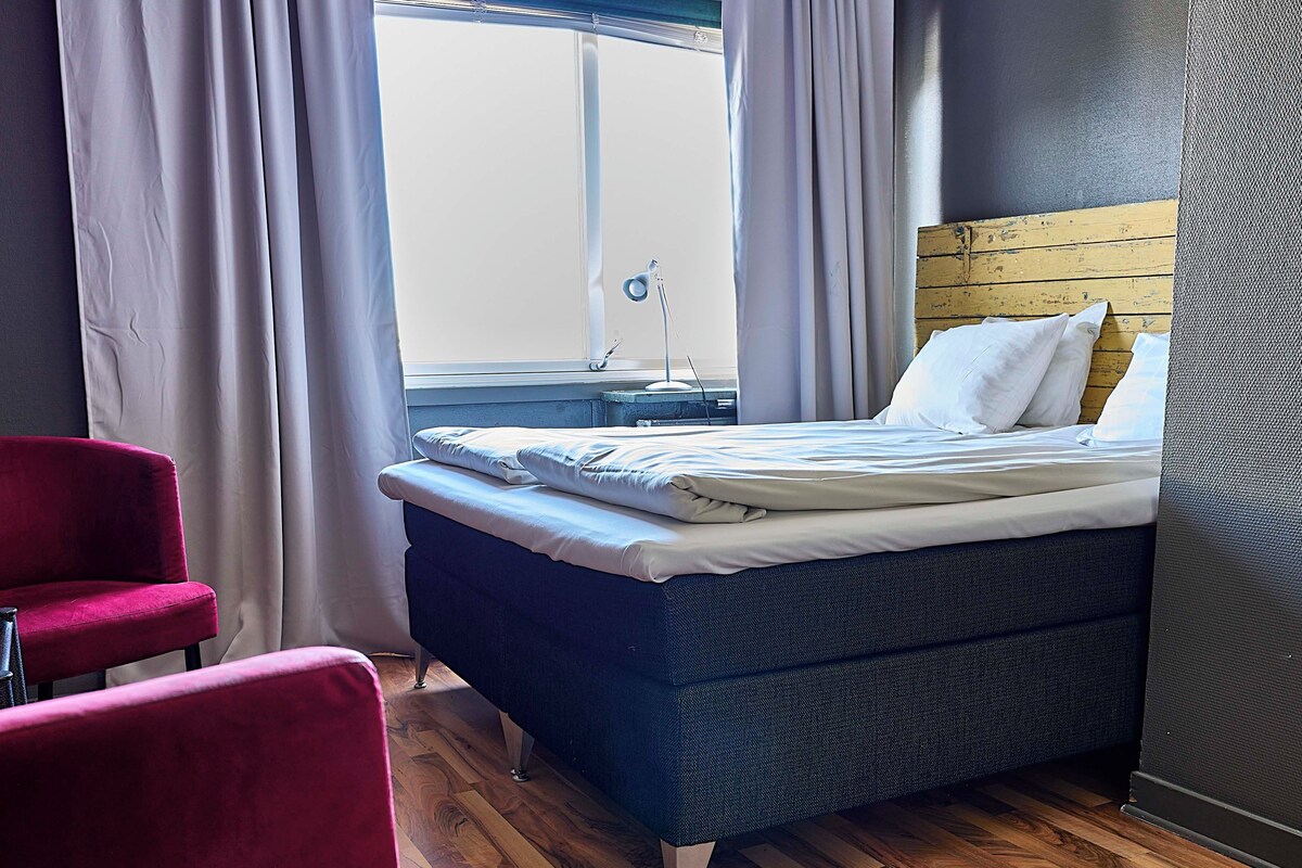 A room with a bed, a red chair, and a wooden floor.