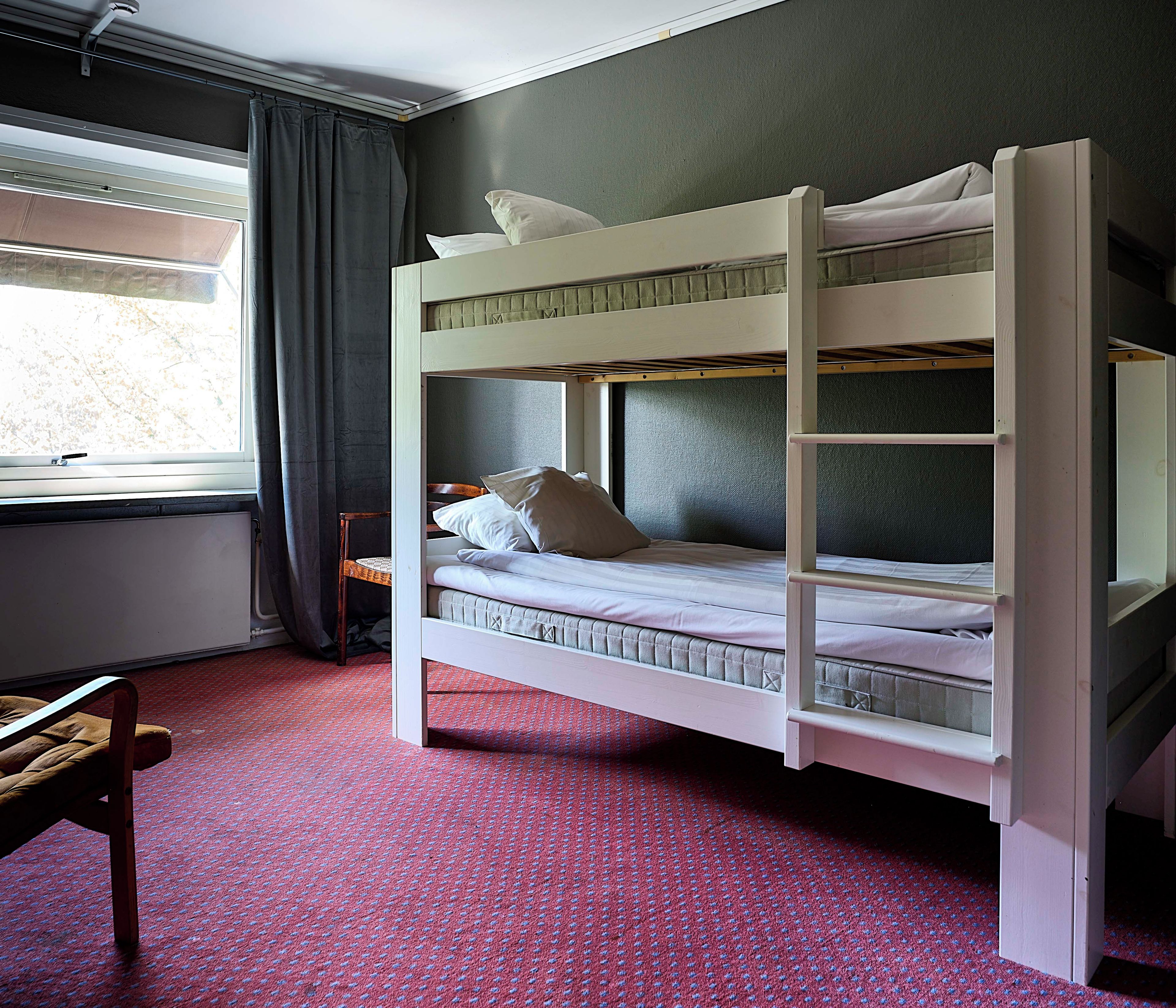 A bunk bed with a window, a chair, and a patterned carpet.