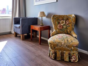 A room with a floral armchair, a dark armchair, a wooden side table with a lamp, and a radiator. - Saga Hotell AB (Borlange)