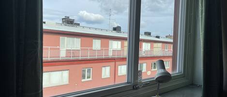 A window with a view of a red building with balconies and a white lamp on the windowsill.