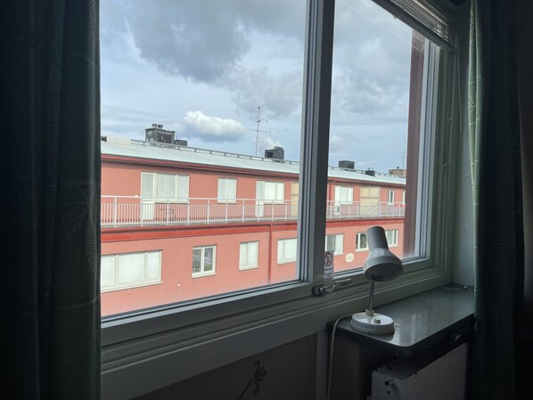 Una ventana con vista a un edificio rojo con balcones y una lámpara blanca en el alféizar.