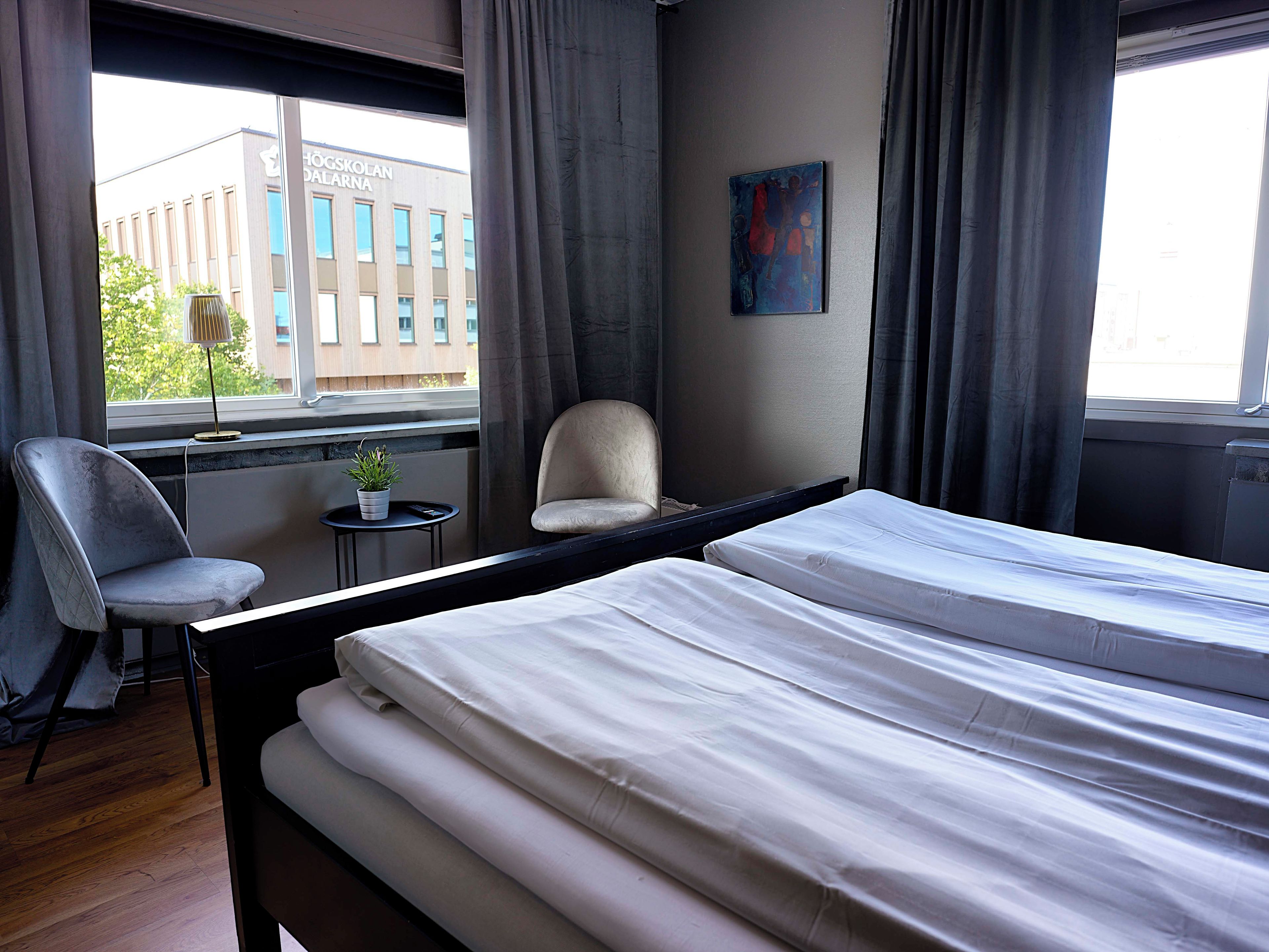 Habitación de hotel con una cama, una silla, una mesita con una planta y vista a un edificio.