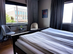 A hotel room with a bed, a chair, a small table with a plant, and a view of a building outside. - Saga Hotell AB (Borlange)