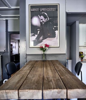 A dining area with a wooden table, chairs, a framed picture on the wall, and a vase with flowers. - Saga Hotell AB (Borlange)