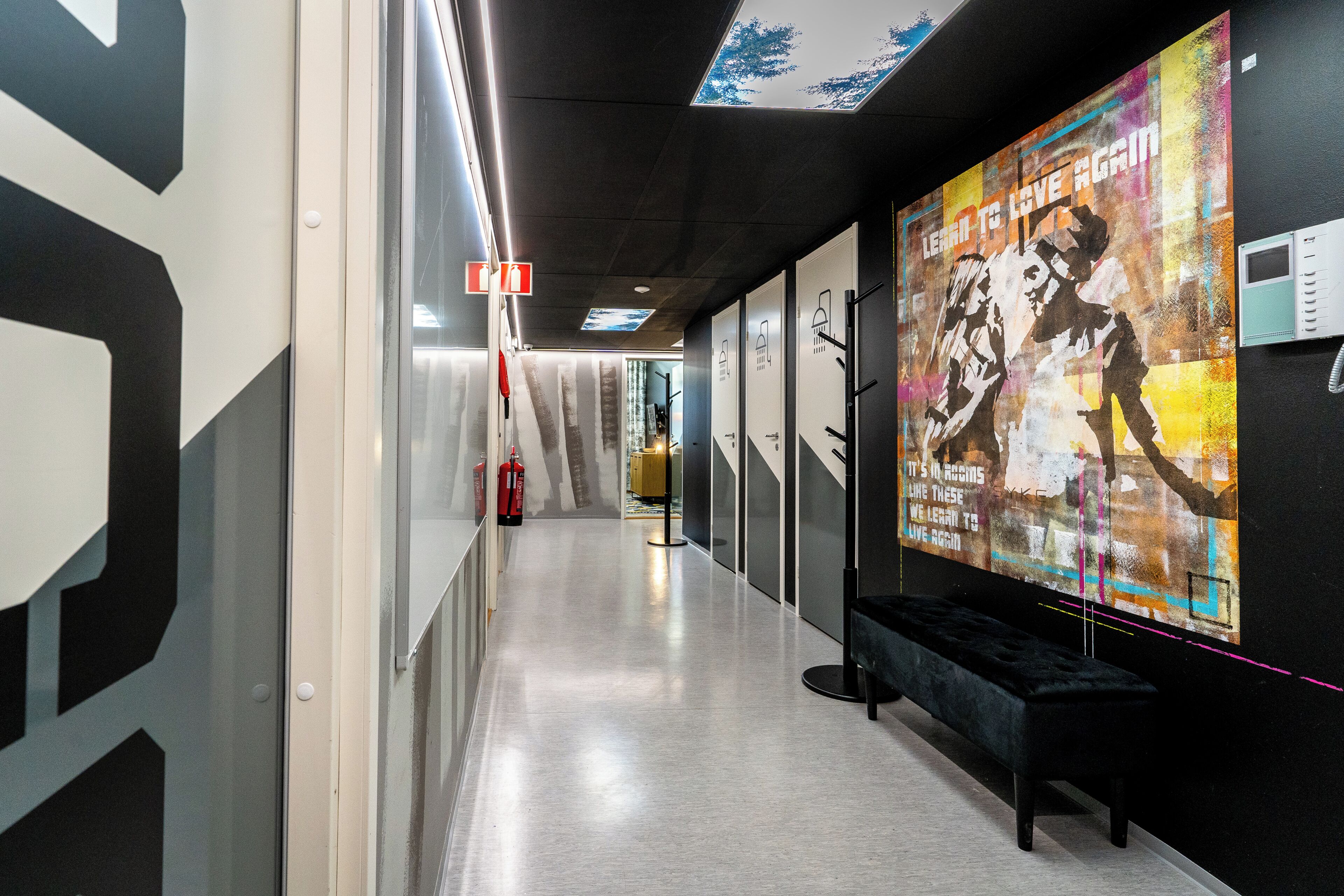 A corridor with fire extinguishers, a bench, and a wall with a poster.