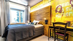 A hotel room with a bed, a desk, and a chair. There is a window with curtains, a wall with a wooden panel design, and a wall with a poster. - Time Hostel NOVA (Jyväskylä)