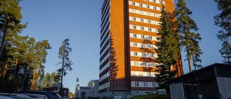 A multi-story building with a brick facade, parking lot, and surrounding trees.