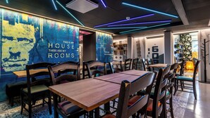 A modern interior with a dining area featuring wooden tables and chairs, a wall with a cityscape mural, and blue neon lighting. - Time Hostel NOVA (Jyväskylä)