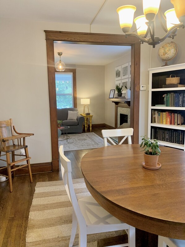 A dining area with a wooden table, white chairs, and a potted plant. There is a bookshelf with books and a globe in the background.
