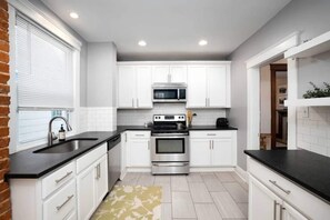A modern kitchen with white cabinets, a black countertop, stainless steel appliances, and a window with blinds.