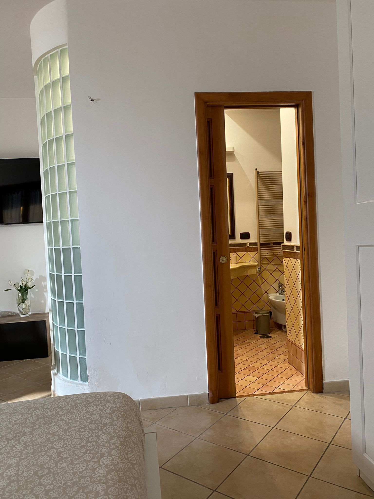 Ein Zimmer mit einem Bett, einer Glaskabine, einer Holztür zu einem Badezimmer mit Waschbecken und Toilette.