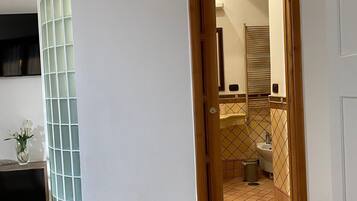 Ein Zimmer mit einem Bett, einer Glaskabine, einer Holztür zu einem Badezimmer mit Waschbecken und Toilette.