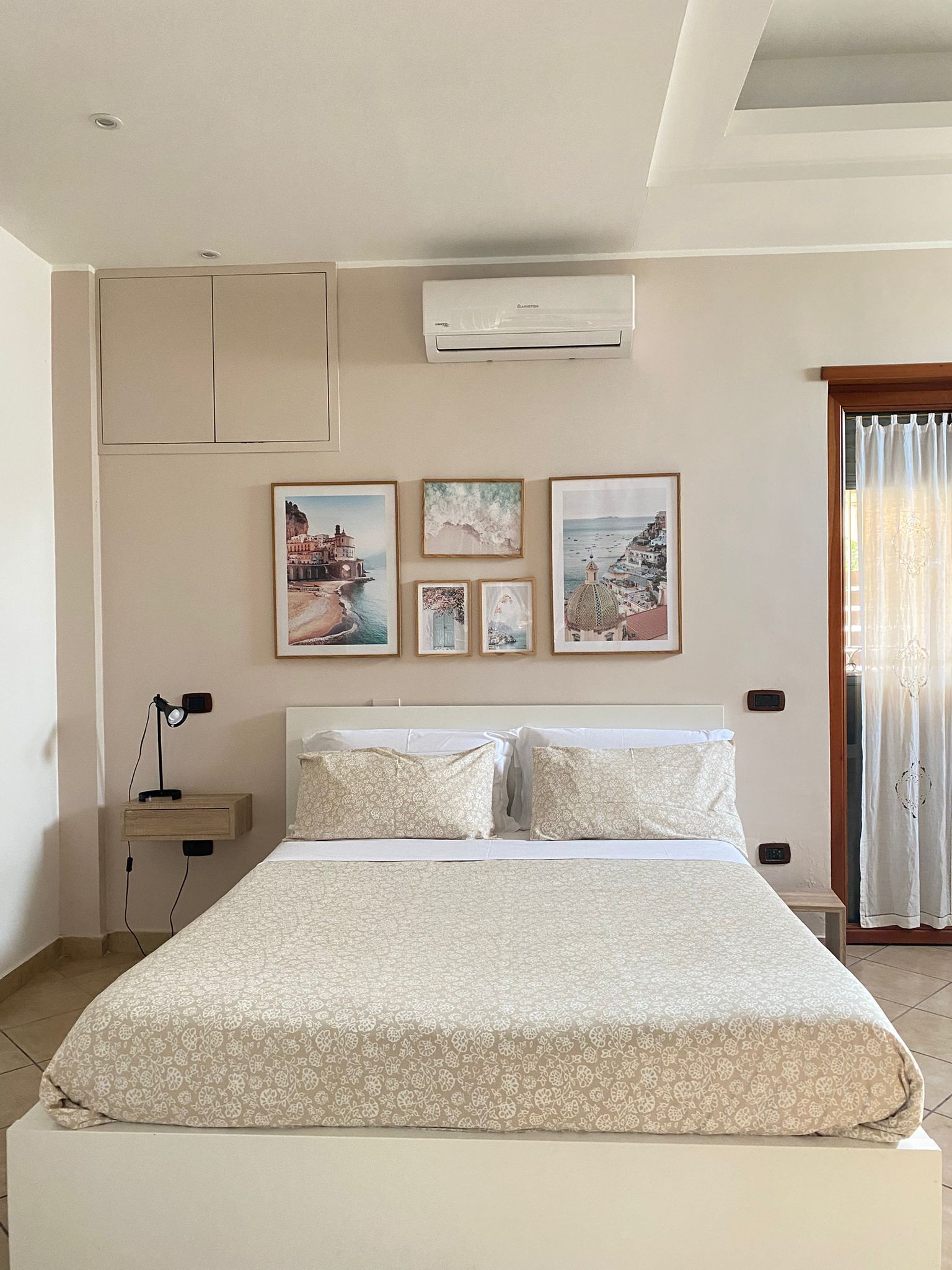 A bedroom with a bed, a nightstand, an air conditioner, and wall-mounted artwork.