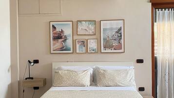 A bedroom with a bed, a nightstand, an air conditioner, and wall-mounted artwork.