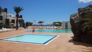 A pool area with two pools, sun loungers, and umbrellas. - Stunning front line 2 bedroom apartment. (Tías)