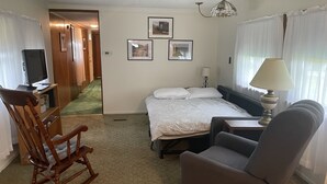 A hotel room with a bed, a desk, a chair, a TV, and a lamp. - Pap's Place (Rockwood)