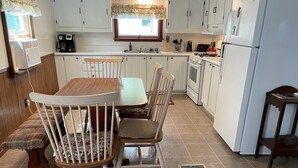 A kitchen with white cabinets, a wooden dining table, and chairs. There is a window with a floral curtain, a sink, and a stove. - Pap's Place (Rockwood)