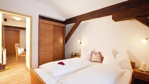 Une chambre d’hôtel avec un plafond en bois, un lit recouvert de draps blancs, une table de chevet avec une bougie et une armoire en bois.