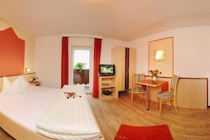Habitación de hotel con cama, televisión, escritorio con silla y ventana con cortinas.